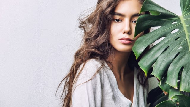 Young beautiful girl model Asian brunette with long hair posing in Studio with tropical plant on isolated background